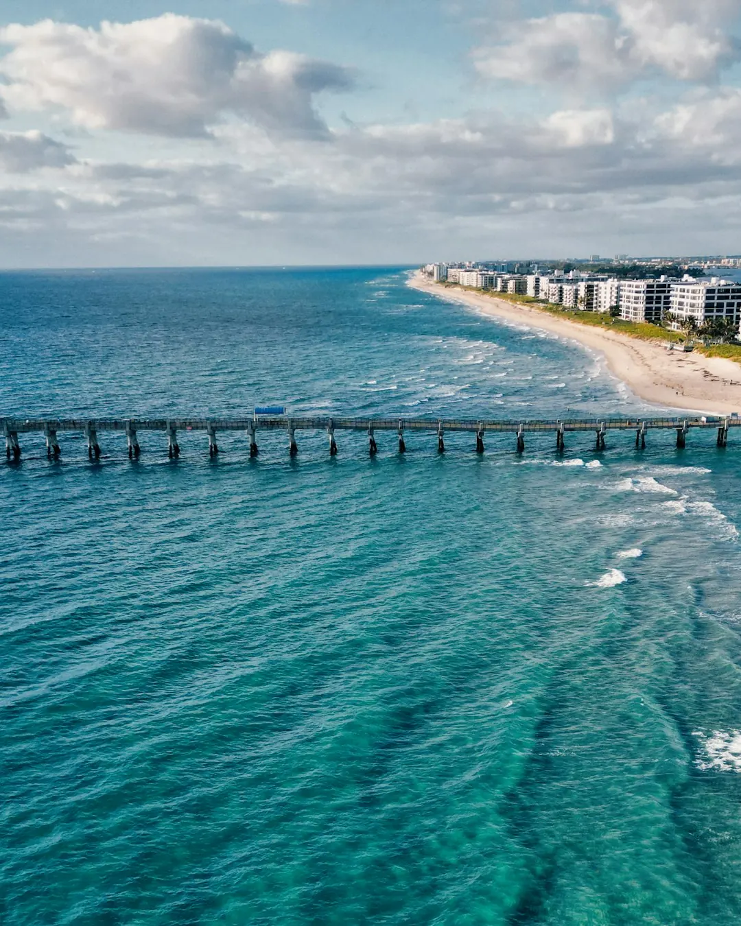 Aerial view of a pier reaching into turquoise water off Palm Beach